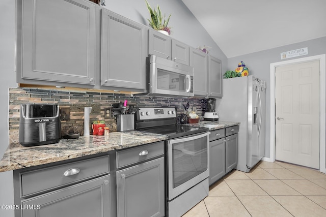 kitchen with light tile patterned flooring, gray cabinetry, stainless steel appliances, vaulted ceiling, and backsplash