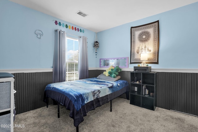 bedroom with a wainscoted wall, light carpet, and visible vents