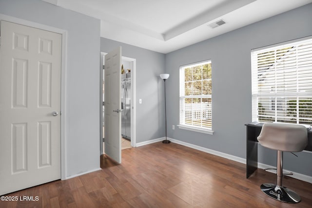 office area with a tray ceiling, wood finished floors, visible vents, and baseboards