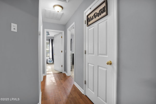 hall with baseboards, wood finished floors, visible vents, and attic access