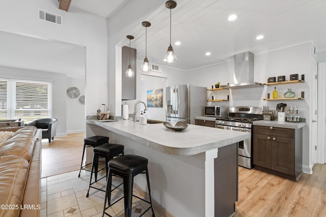 kitchen featuring wall chimney exhaust hood, a kitchen bar, sink, decorative light fixtures, and appliances with stainless steel finishes