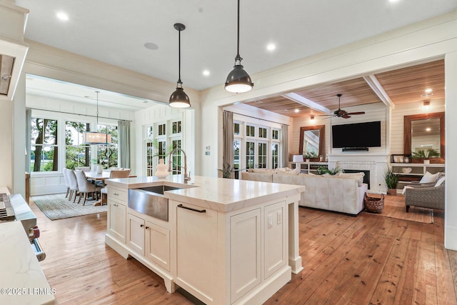24 Carrier Blf, Bluffton, SC 29909 - kitchen with light wood-style floors, ceiling fan, hanging light fixtures, a center island with sink, and light stone counters