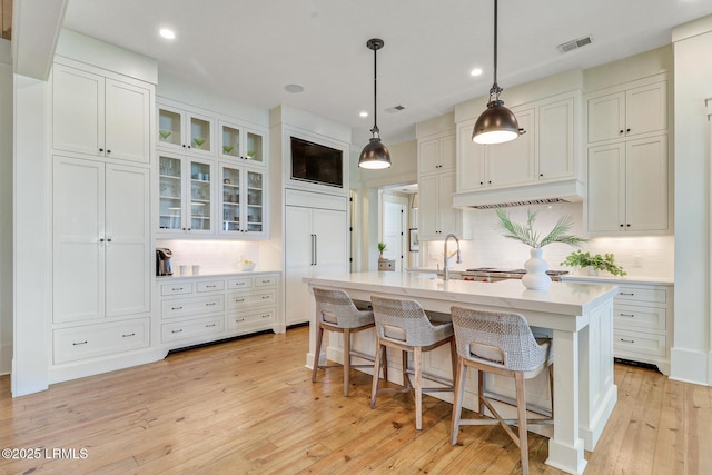 24 Carrier Blf, Bluffton, SC 29909 - kitchen featuring under cabinet range hood, light countertops, light wood-style floors, tasteful backsplash, and a kitchen breakfast bar