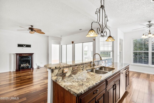 kitchen featuring pendant lighting, sink, light stone counters, an island with sink, and dark hardwood / wood-style flooring