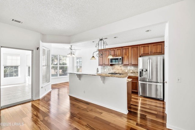 kitchen with appliances with stainless steel finishes, a breakfast bar, an island with sink, backsplash, and light stone countertops