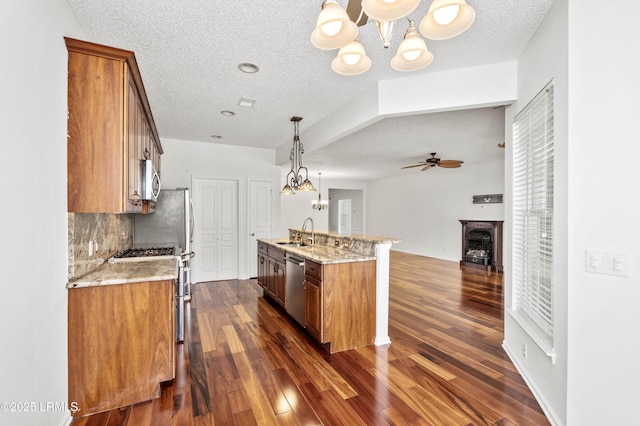 kitchen featuring sink, light stone counters, hanging light fixtures, appliances with stainless steel finishes, and backsplash