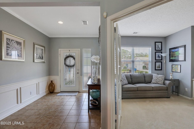 carpeted foyer featuring tile patterned flooring, a textured ceiling, visible vents, and wainscoting