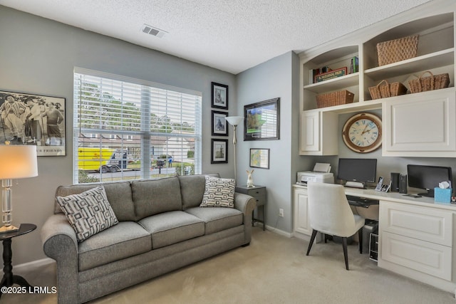 office area featuring visible vents, light carpet, a textured ceiling, baseboards, and built in study area