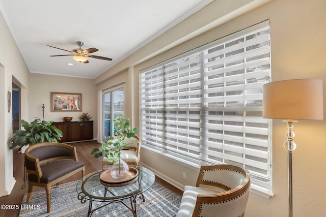 living area with baseboards, wood finished floors, a ceiling fan, and ornamental molding