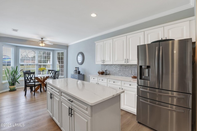 kitchen featuring light wood finished floors, backsplash, crown molding, stainless steel refrigerator with ice dispenser, and a ceiling fan