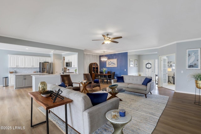 living room with light wood finished floors, a ceiling fan, crown molding, and baseboards