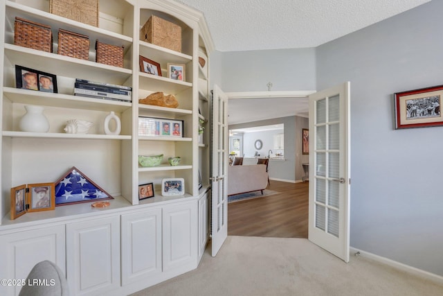 hallway with light colored carpet, french doors, a textured ceiling, and baseboards