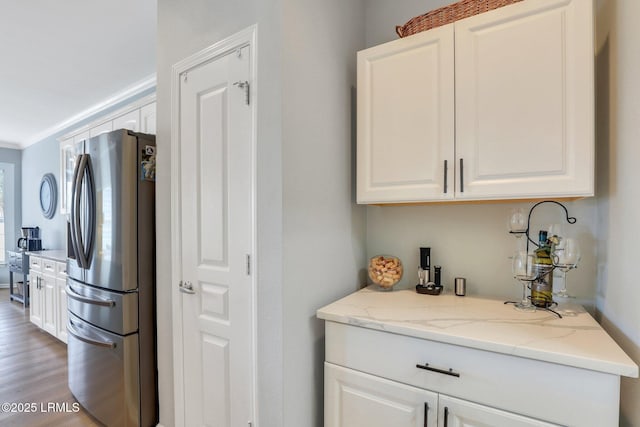 kitchen with white cabinets, light stone countertops, stainless steel refrigerator with ice dispenser, and ornamental molding