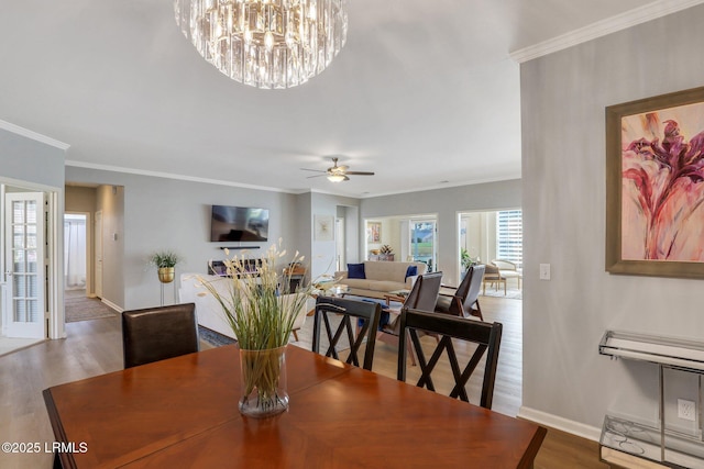 dining space with ceiling fan with notable chandelier, crown molding, baseboards, and wood finished floors