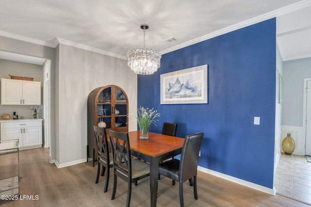 dining room with visible vents, wood finished floors, an inviting chandelier, and ornamental molding