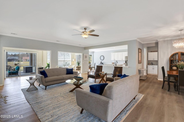 living area featuring visible vents, ceiling fan with notable chandelier, wood finished floors, crown molding, and baseboards