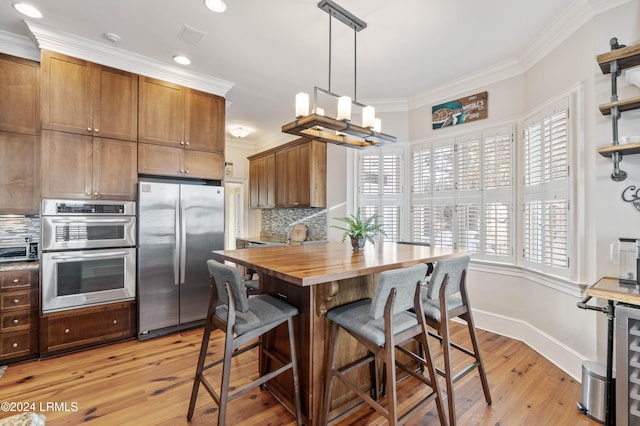 kitchen featuring appliances with stainless steel finishes, wood counters, backsplash, hanging light fixtures, and light wood-type flooring