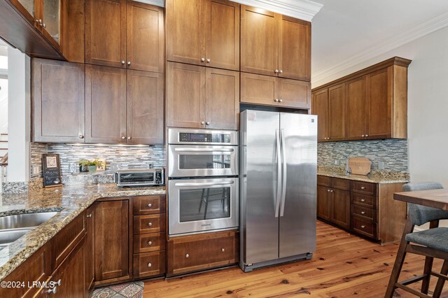 kitchen featuring light hardwood / wood-style flooring, appliances with stainless steel finishes, light stone counters, tasteful backsplash, and ornamental molding