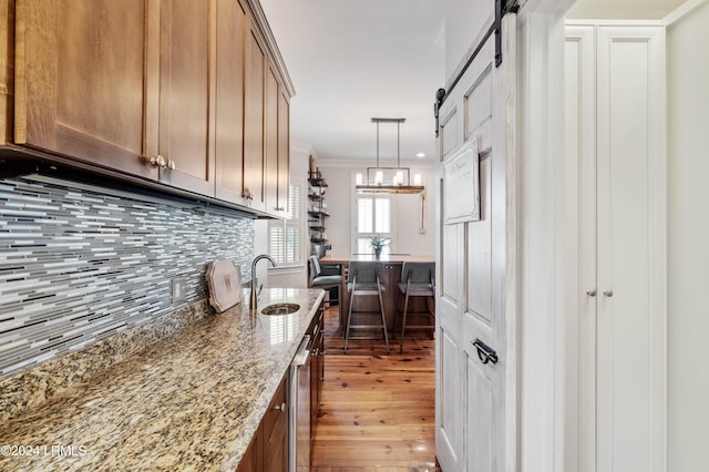 kitchen with sink, light stone counters, crown molding, a barn door, and backsplash