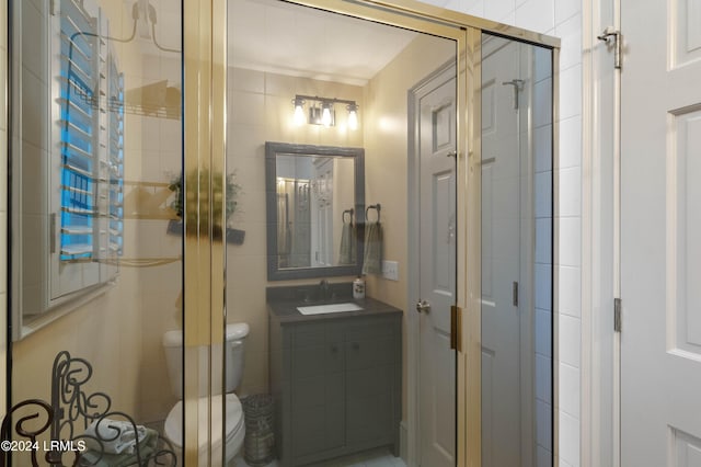 bathroom featuring a shower with door, vanity, and toilet