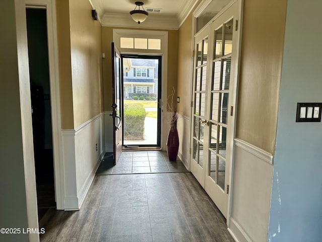 doorway with wood finished floors, a wainscoted wall, visible vents, ornamental molding, and french doors