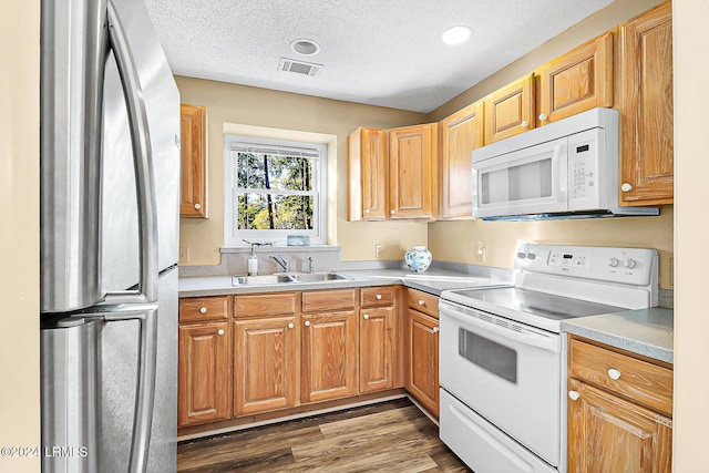 kitchen featuring white appliances, visible vents, wood finished floors, a textured ceiling, and a sink