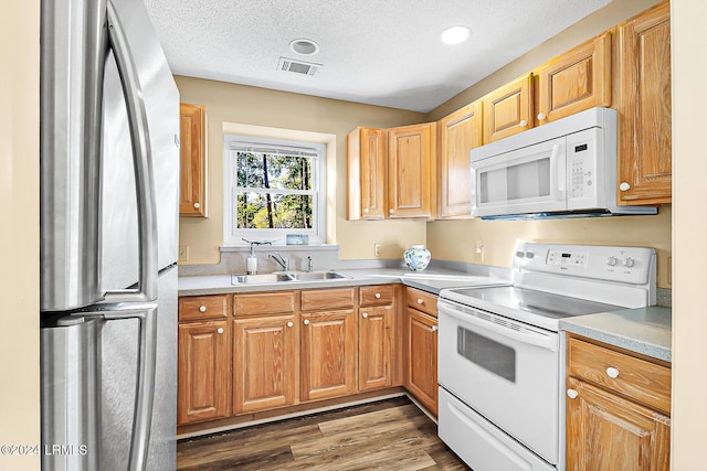 kitchen featuring a textured ceiling, white appliances, wood finished floors, a sink, and visible vents