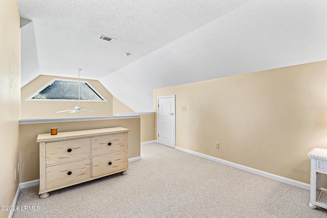 additional living space with a textured ceiling, lofted ceiling, light carpet, visible vents, and baseboards