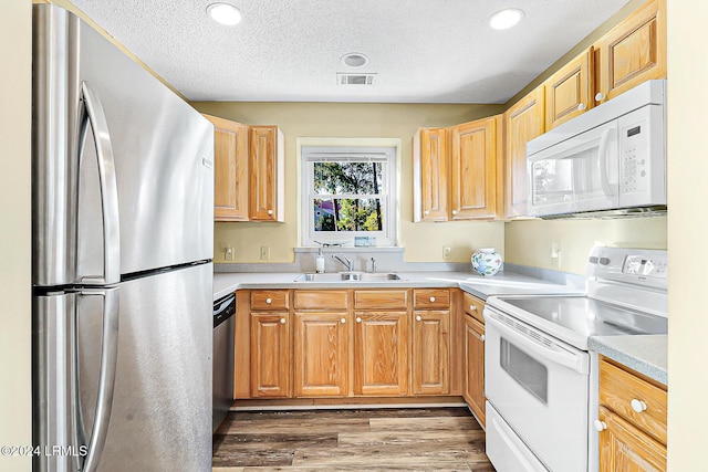 kitchen with stainless steel appliances, light countertops, visible vents, a sink, and wood finished floors