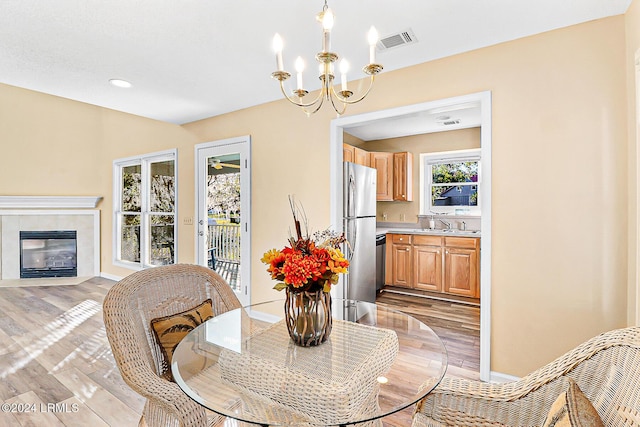 dining room featuring a notable chandelier, visible vents, light wood-style flooring, a tile fireplace, and baseboards