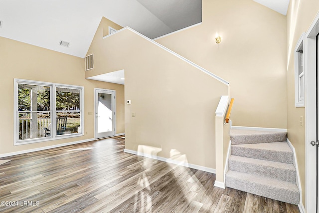 foyer featuring visible vents, stairway, wood finished floors, high vaulted ceiling, and baseboards