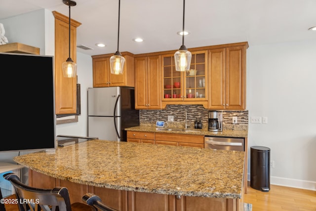 kitchen with sink, light stone counters, tasteful backsplash, hanging light fixtures, and stainless steel appliances