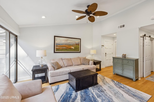 living room featuring lofted ceiling, light hardwood / wood-style flooring, ornamental molding, ceiling fan, and a barn door