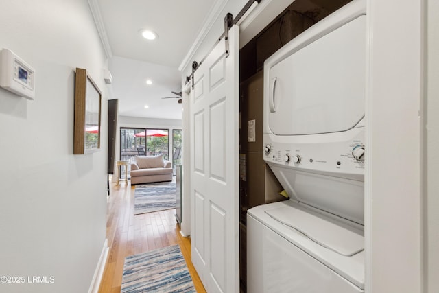 washroom with crown molding, hardwood / wood-style flooring, stacked washer and clothes dryer, and a barn door