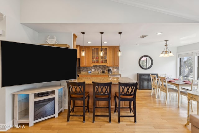 kitchen featuring hanging light fixtures, decorative backsplash, light stone countertops, and light hardwood / wood-style floors