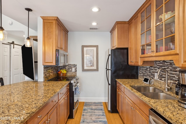 kitchen with pendant lighting, sink, stainless steel appliances, light stone counters, and a barn door