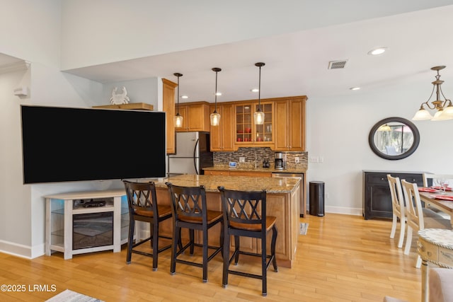 kitchen featuring pendant lighting, appliances with stainless steel finishes, light stone counters, and light wood-type flooring