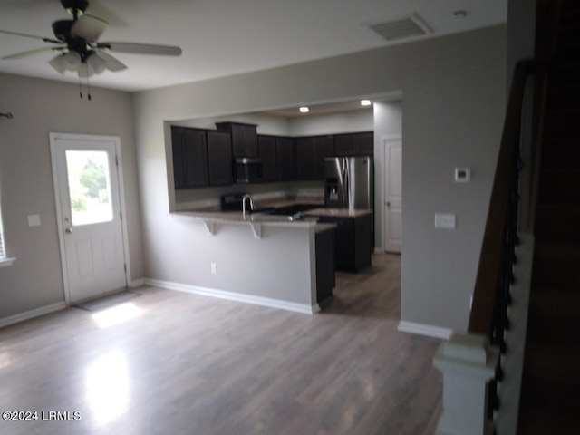 kitchen featuring a kitchen bar, baseboards, wood finished floors, a peninsula, and stainless steel fridge with ice dispenser