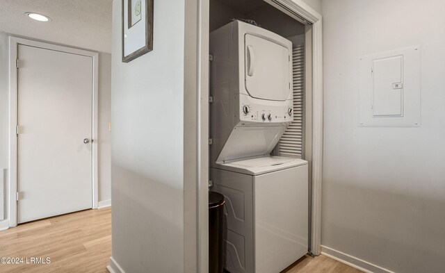 laundry room with stacked washer / dryer, electric panel, and light hardwood / wood-style floors