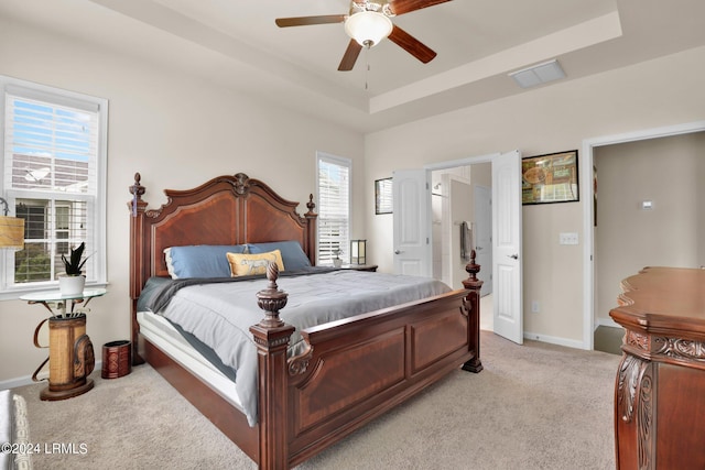 bedroom featuring light colored carpet, a raised ceiling, ceiling fan, and ensuite bathroom