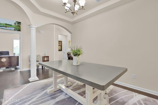 dining area featuring an inviting chandelier, a tray ceiling, dark hardwood / wood-style floors, and decorative columns