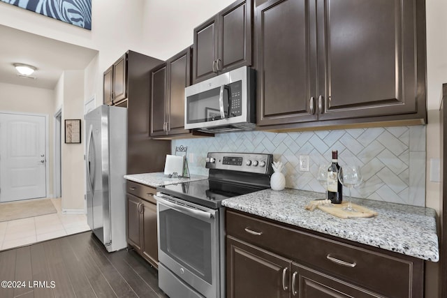 kitchen featuring backsplash, dark hardwood / wood-style flooring, stainless steel appliances, light stone countertops, and dark brown cabinets