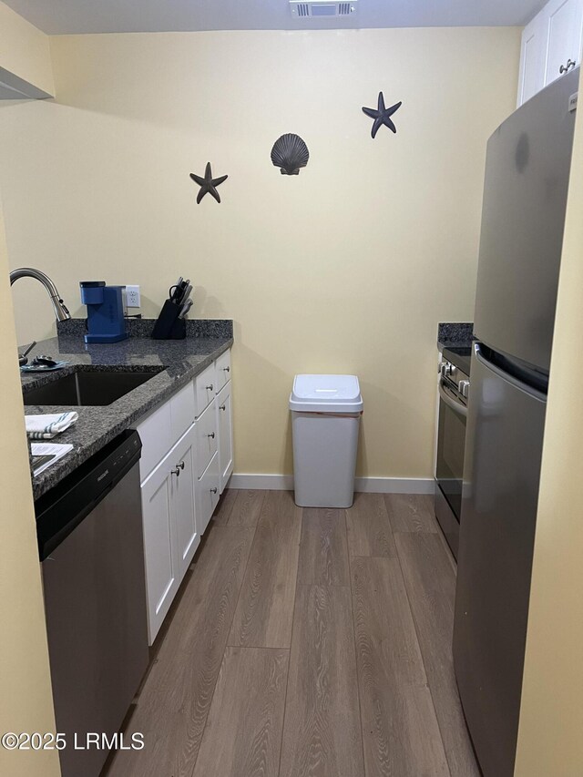 kitchen featuring stainless steel appliances, sink, dark stone counters, and white cabinets