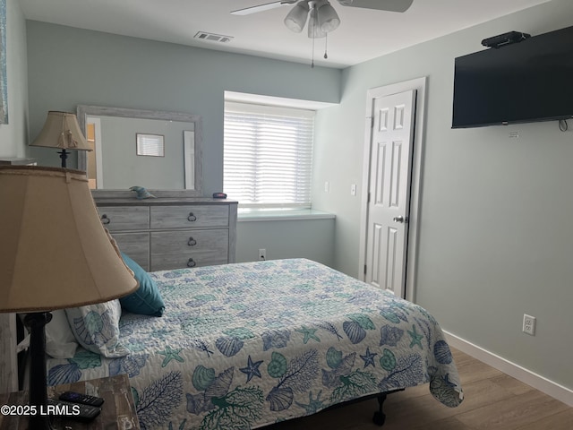 bedroom featuring a ceiling fan, visible vents, wood finished floors, and baseboards