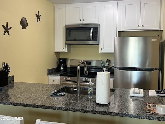 kitchen with white cabinetry, stainless steel appliances, and dark stone countertops