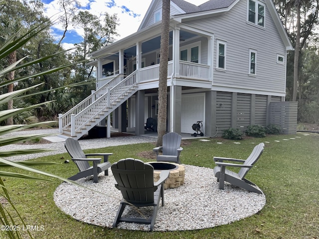 rear view of property with an attached garage, stairs, a fire pit, and a lawn