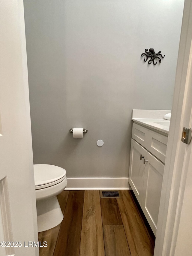 bathroom featuring visible vents, toilet, vanity, wood finished floors, and baseboards