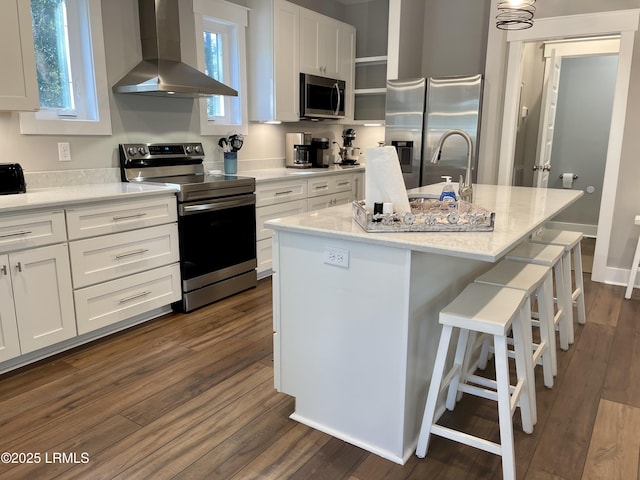 kitchen featuring wall chimney exhaust hood, appliances with stainless steel finishes, an island with sink, and white cabinets