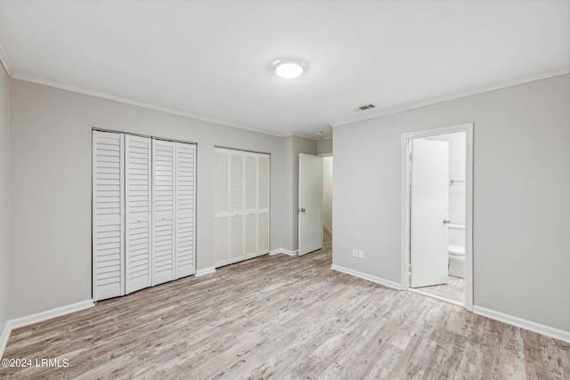 unfurnished bedroom featuring multiple closets, ornamental molding, ensuite bathroom, and light hardwood / wood-style floors