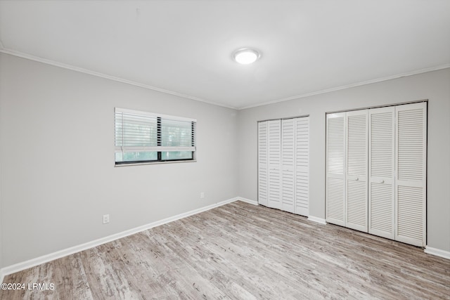 unfurnished bedroom featuring multiple closets, ornamental molding, and light hardwood / wood-style flooring